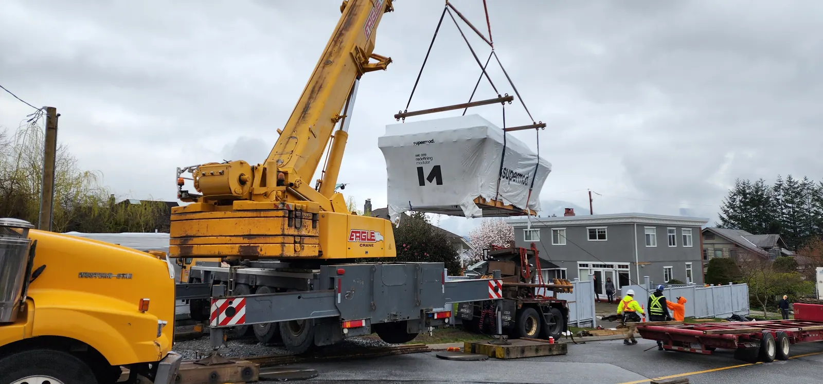 Crane lifting a wrapped volumetric module into place on a residential site
