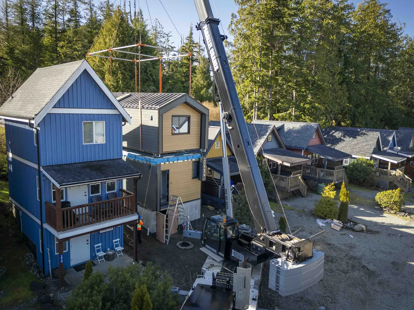 Crane placing a modular cottage between neighbouring homes in Ucluelet